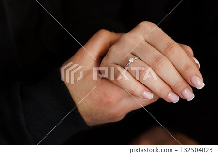 Romantic Engagement: Hands Holding Diamond Ring, Couple, Love, Proposal, White Gold, Close-up, Black Background, Intimate Moment, Celebration. Romantic Engagement: Hands Holding Diamond Ring, Couple, Love, Proposal, White Gold, Close-up, Black Background, Intimate Moment, Celebration. 132504023