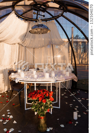 Romantic Dinner Setup in Geodesic Dome Tent with Rose Petals, Candles, and Draped White Fabric Intimate Evening Scene with Warm Lighting. 132504070