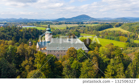 Lemberk Castle is showcased from a bird's-eye view, surrounded by lush greenery and rolling hills. The sky is clear, highlighting the castle's impressive structure and scenic landscape. 132506327