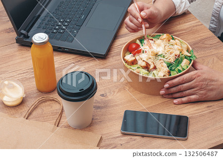 a woman is working on a laptop at home, there is food on the table, salad, coffee and juice, delivery, 132506487