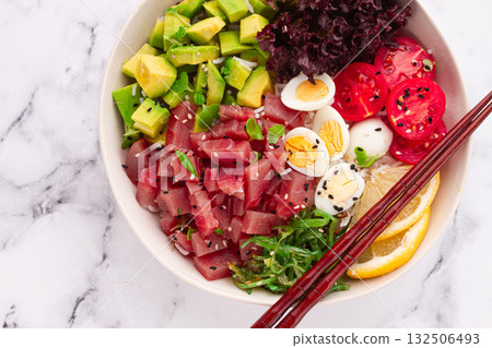 Fresh poke bowl, with tuna, avocado, and vegetables, served on a white plate Fresh poke bowl, with tuna, avocado, and vegetables, served on a white plate 132506493