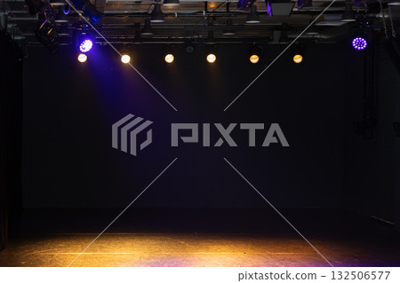 An empty stage with a dark backdrop and warm overhead lights. An empty stage with a dark backdrop and warm overhead lights. 132506577