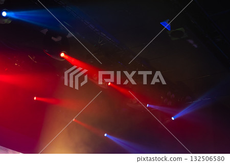 Energetic concert scene featuring red and blue spotlights cutting through haze 132506580