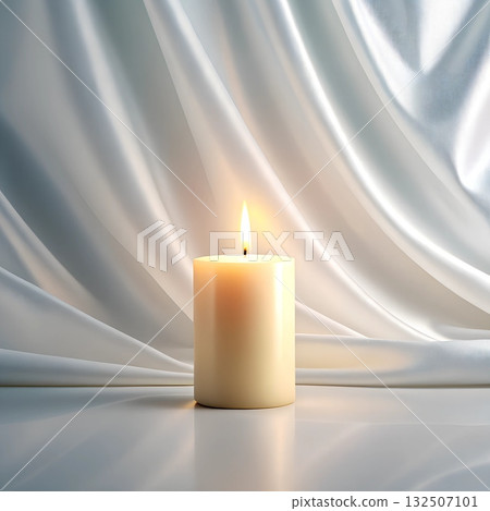 A lit cream candle rests on a reflective surface against flowing white fabric 132507101
