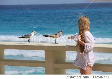 Young girl with long blonde hair extends her hand to seagulls 132507467