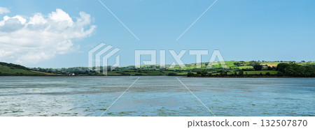 Scenic waters of West Cork, Ireland, meet the lush green landscape under a dramatic cloudy sky during the day. 132507870