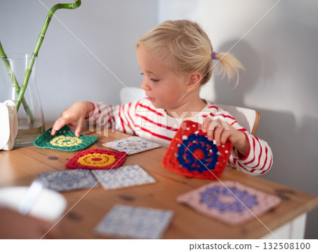 4 year old girl sitting at the table arranging knitted squares. autistic play 132508100