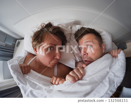 Middle aged couple lying under the blanket looking surprised. problems in life 132508151