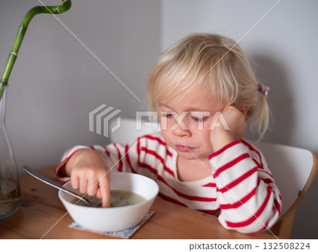 Blonde 4 year old girl touching soup with her finger, refusing to eat Blonde 4 year old girl touching soup with her finger, refusing to eat 132508224