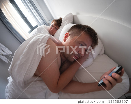 Man using his phone at night while his wife sleeps beside him, bad habit and screen addiction Man using his phone at night while his wife sleeps beside him, bad habit and screen addiction 132508307