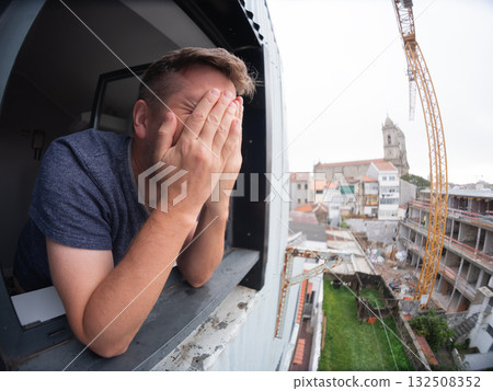Man angrily staring at a noisy construction site outside his apartment window Man angrily staring at a noisy construction site outside his apartment window 132508352