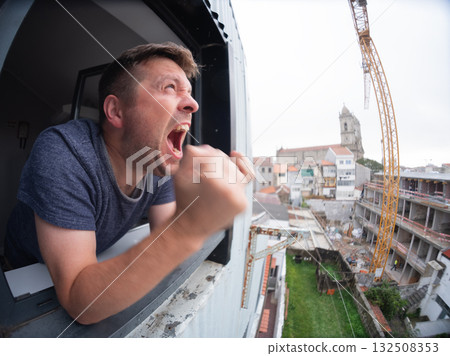 Man angrily staring at a noisy construction site outside his apartment window Man angrily staring at a noisy construction site outside his apartment window 132508353