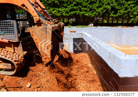 Construction worker operates excavator to load soil into building foundation Construction worker operates excavator to load soil into building foundation 132508377