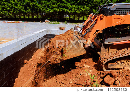 Excavator pouring dirt from ground as construction progresses on building foundation Excavator pouring dirt from ground as construction progresses on building foundation 132508380