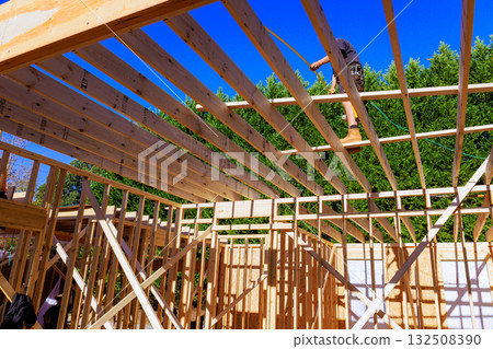 Construction worker carefully measures installs roof beams in new home while framing is underway. 132508390