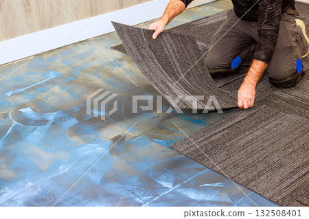 Handy man lays carpet tiles on old floor in living room, preparing for an updated refreshed space. 132508401