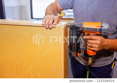 Carpenter is using air nail gun to assemble wooden cabinet drawer section Carpenter is using air nail gun to assemble wooden cabinet drawer section 132508424