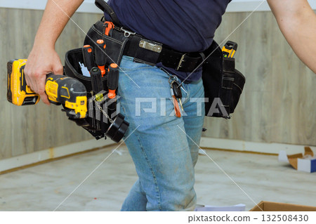 Construction worker is actively using power drill in home under renovation, using tool belt equipment. 132508430