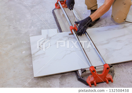 Carpenter is carefully cutting large tile with manual tile cutter in newly remodeled area of home. Carpenter is carefully cutting large tile with manual tile cutter in newly remodeled area of home. 132508438