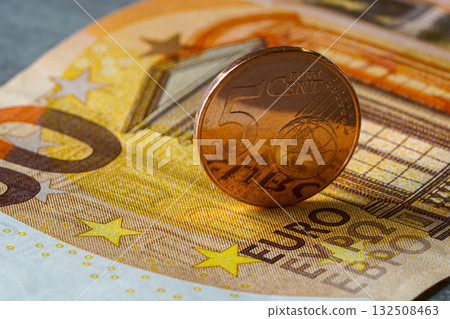 Five euro cent coin standing on fifty euro banknote, symbolizing savings, finance, and economy Five euro cent coin standing on fifty euro banknote, symbolizing savings, finance, and economy 132508463