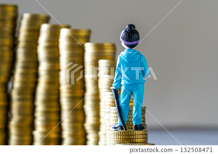 Toy figure in blue tracksuit standing on gold coins symbolizing wealth, ambition, and economic growth Toy figure in blue tracksuit standing on gold coins symbolizing wealth, ambition, and economic growth 132508471