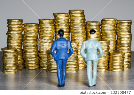 Two miniature businessmen standing before stacks of gold coins symbolizing wealth and financial growth Two miniature businessmen standing before stacks of gold coins symbolizing wealth and financial growth 132508477