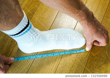 Measuring foot length in centimeters and inches with ruler on wooden floor for shoe size fitting 132508490