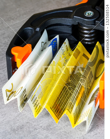 Euro banknotes squeezed in black and orange clamp symbolizing financial stress and inflation crisis 132508514