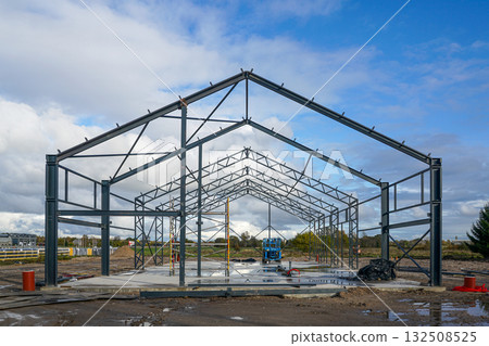 Steel structure frame of warehouse building under construction with scaffolding and blue lift 132508525