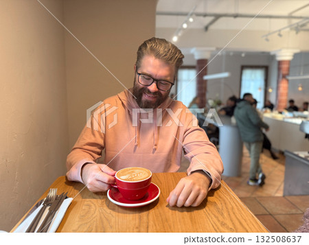 Man enjoying latte in modern cafe. Everyday relaxation, morning ritual and cozy coffee culture in urban lifestyle setting. 132508637