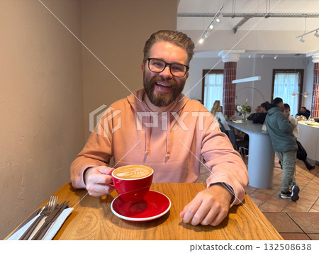 Man smiling with cup of coffee in modern cafe. Expression of joy, warmth and everyday connection over morning beverage. Man smiling with cup of coffee in modern cafe. Expression of joy, warmth and everyday connection over morning beverage. 132508638