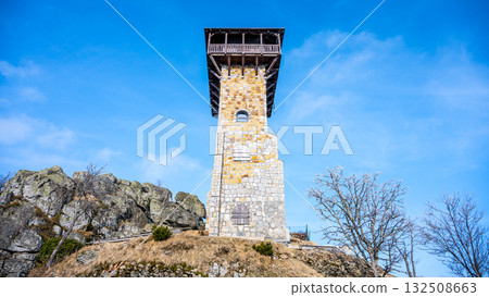 The lookout tower stands tall on Wysoki Kamien surrounded by rocky terrain and trees in the Jizera Mountains of Poland. Clear blue skies enhance the scenery, inviting exploration. The lookout tower stands tall on Wysoki Kamien surrounded by rocky terrain and trees in the Jizera Mountains of Poland. Clear blue skies enhance the scenery, inviting exploration. 132508663