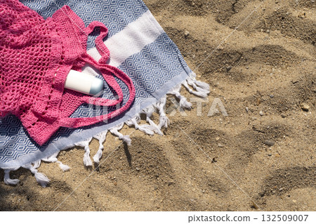 Flat lay showing SPF cream peeking out of a pink mesh bag on a beach towel. Flat lay showing SPF cream peeking out of a pink mesh bag on a beach towel. 132509007
