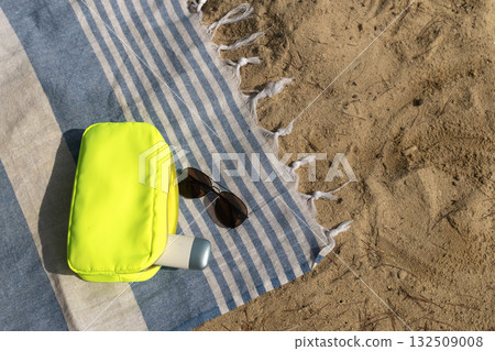 Neon makeup bag with SPF cream and sunglasses on a beach towel. 132509008