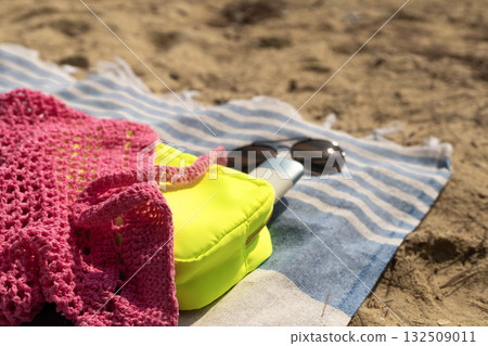Pink mesh bag, neon makeup bag with SPF cream and sunglasses on a beach towel on the sand. Pink mesh bag, neon makeup bag with SPF cream and sunglasses on a beach towel on the sand. 132509011