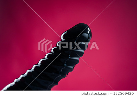 Lube pouring on black dildo on pink background.  132509420