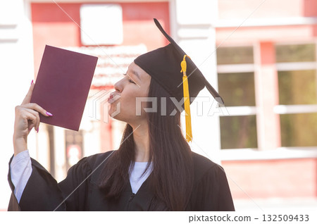 Portrait of young asian woman in graduation gown holding diploma.  132509433