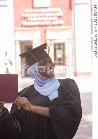 African woman in hijab and graduation gown holding diploma. African woman in hijab and graduation gown holding diploma. 132509434