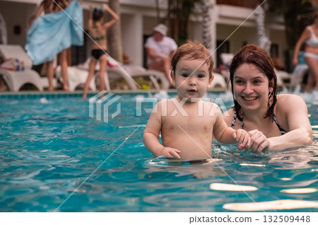 Caucasian woman holds her son while swimming in a pool on vacation. Mom teaches little boy to swim. Caucasian woman holds her son while swimming in a pool on vacation. Mom teaches little boy to swim. 132509448