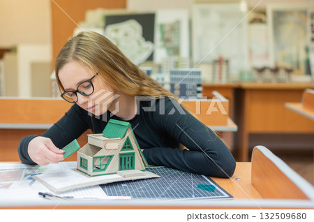 Caucasian young woman making a model of a building. Student of the construction university. Caucasian young woman making a model of a building. Student of the construction university. 132509680