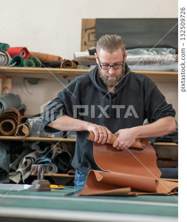 Caucasian bearded man working as a tanner in a workshop.  132509726