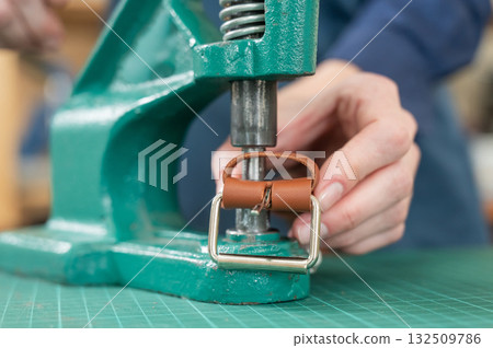 A woman attaches accessories to a leather belt. Leatherworker's workshop. A woman attaches accessories to a leather belt. Leatherworker's workshop. 132509786
