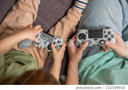 Caucasian woman teaches her little son to play console. Joystick in hands. Caucasian woman teaches her little son to play console. Joystick in hands. 132509916