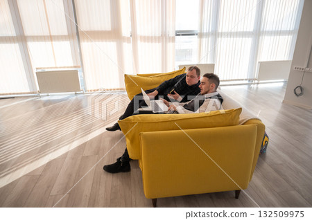 Two Caucasian men discussing work on a laptop while sitting on a sofa. Modern office. Two Caucasian men discussing work on a laptop while sitting on a sofa. Modern office. 132509975