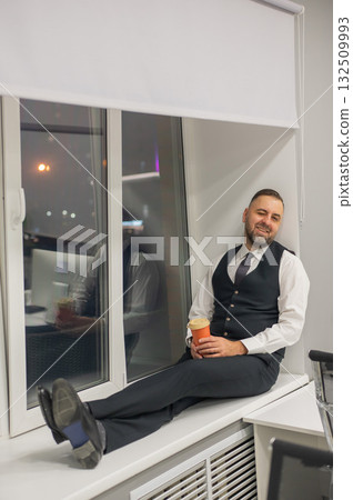 Thoughtful Caucasian man sitting on windowsill in office. Thoughtful Caucasian man sitting on windowsill in office. 132509993