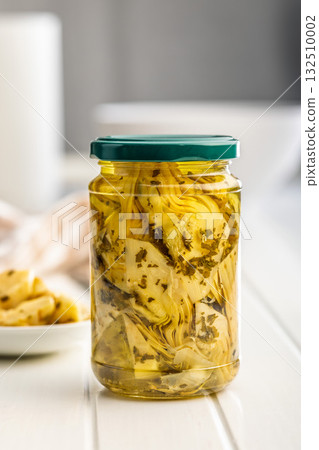 Pickled artichoke in jar on white table. Pickled artichoke in jar on white table. 132510002