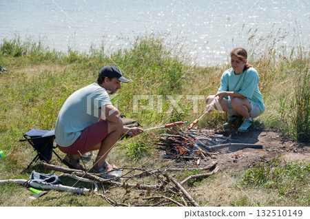 Caucasian couple roasting sausages over a fire.  132510149