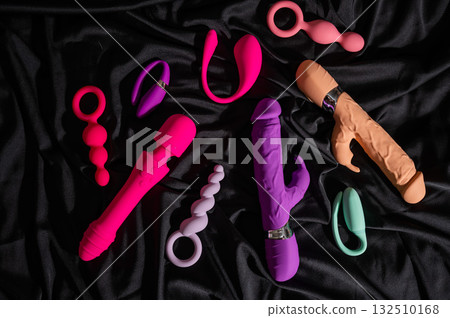 Collection of sex toys on a black sheet. Top view of various vibrators.  132510168