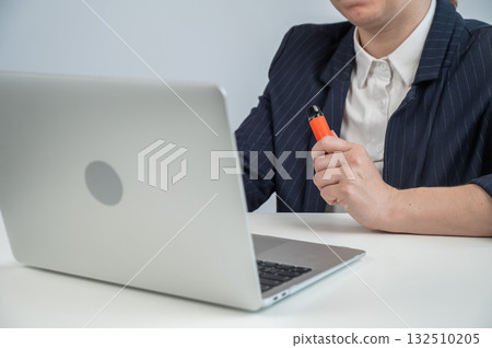 Faceless businesswoman smokes disposable vape and works on laptop.  132510205
