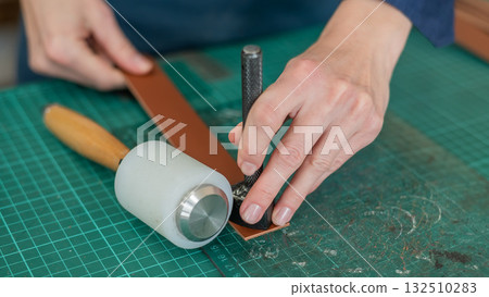 Woman tanner processes the edges of a leather belt in a workshop.  132510283